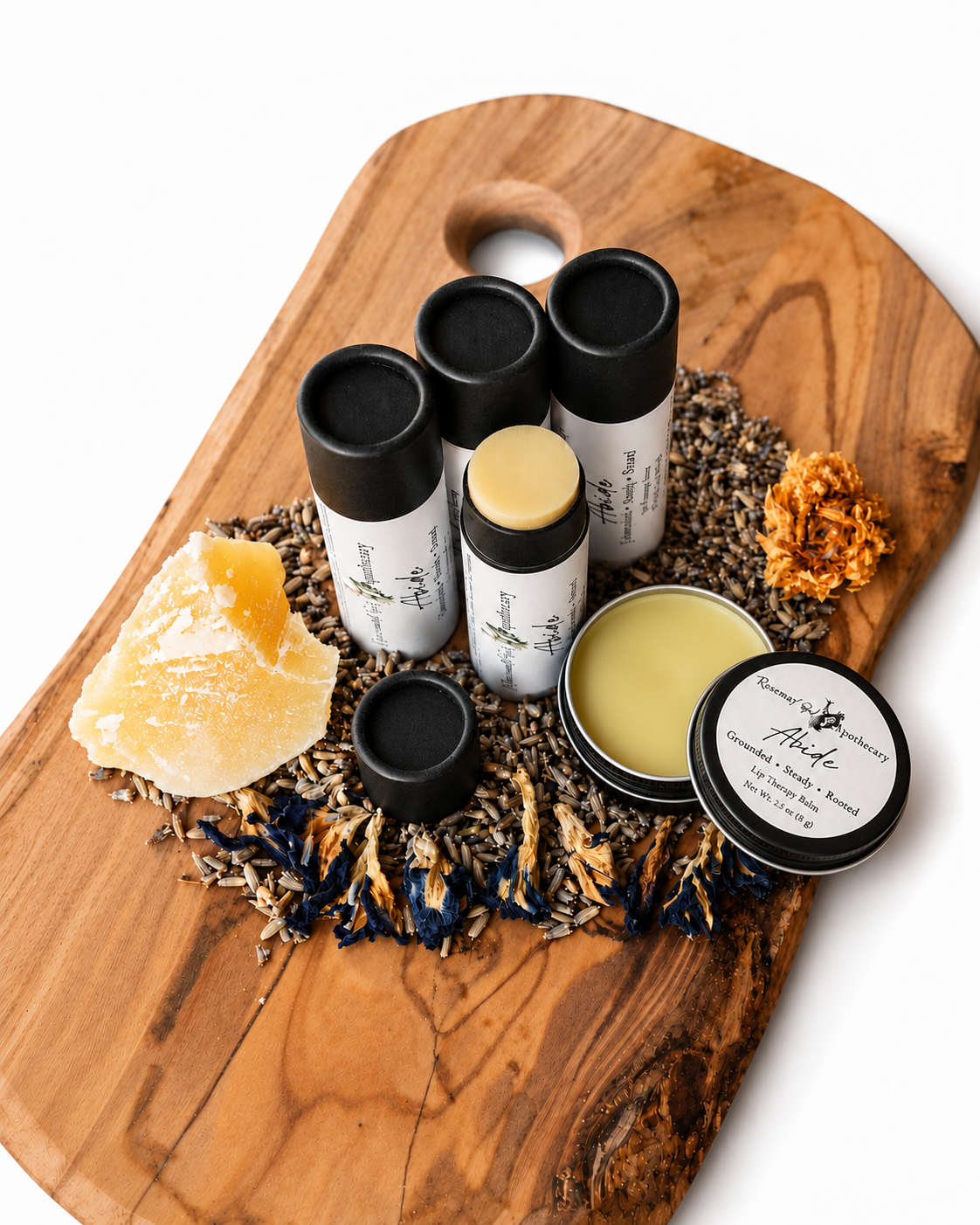 Open Abide herbal tallow lip balm tin with its labeled lid beside paper tubes and dried botanicals.