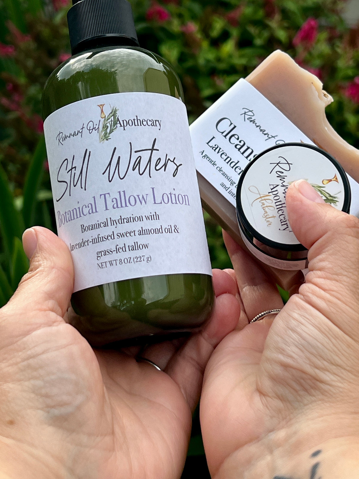 Hand holding Still Waters Botanical Tallow Lotion in a green pump bottle alongside two other handcrafted skincare products from Remnant Oil Apothecary.